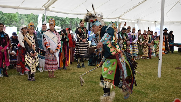 Un homme en tenue traditionnelle danse sous un grand chapiteau blanc.