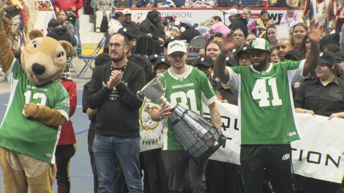 Un joueur des Roughriders tient la Coupe Grey accompagné d'autres membres de sa formation.