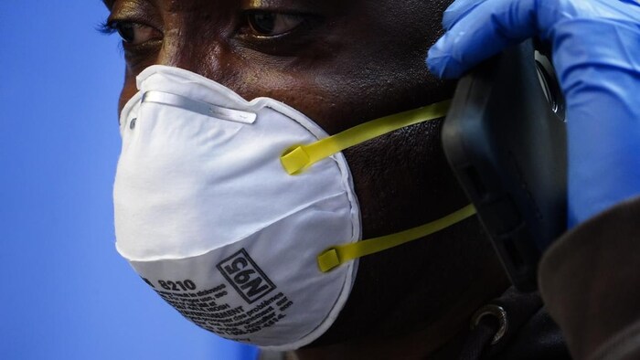 A nurse wearing a N95 mask and gloves speaks on the phone.