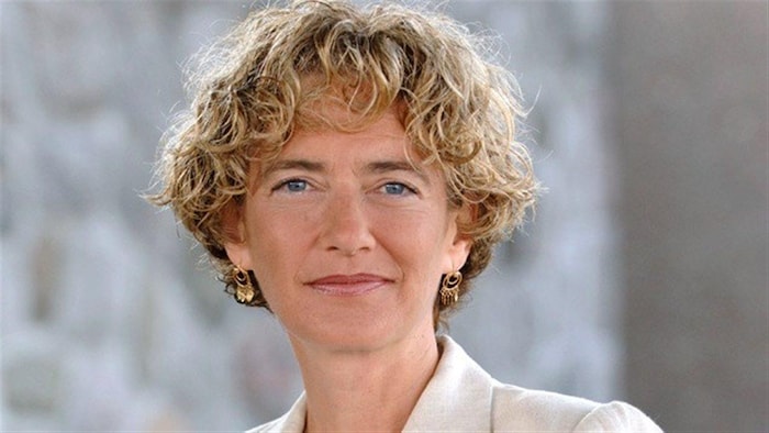 Une femme aux cheveux blonds, frisés et courts regarde la caméra
