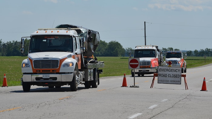 Des dépanneuses transportant les véhicules accidentés quittent les lieux d'une collision mortelle entre deux voitures dans le canton de Mapleton.