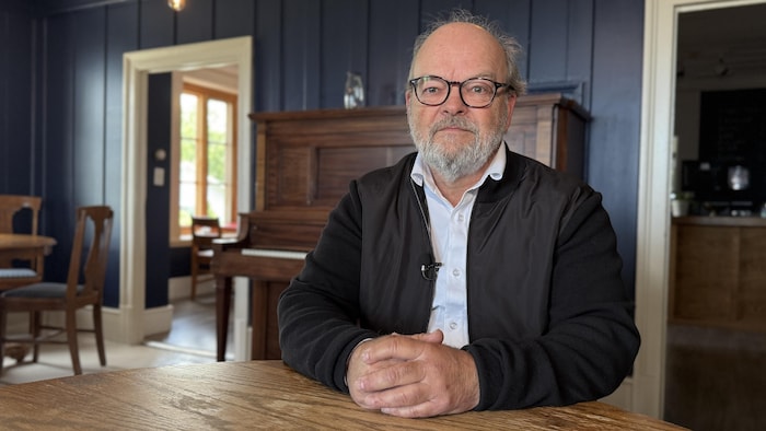Le préfet assis à une table. Il est dans une salle à manger où se trouve un piano.