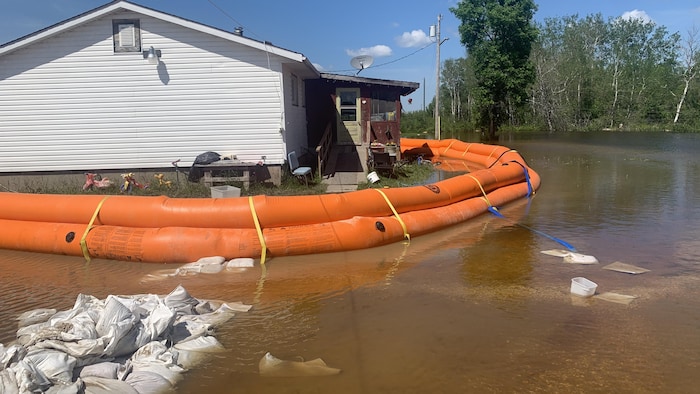 Une maison est entourée d'une digue orange et la digue de sacs de sable tout près se trouve sous l'eau, dans la Première Nation de Peguis, le 26 juin 2022.