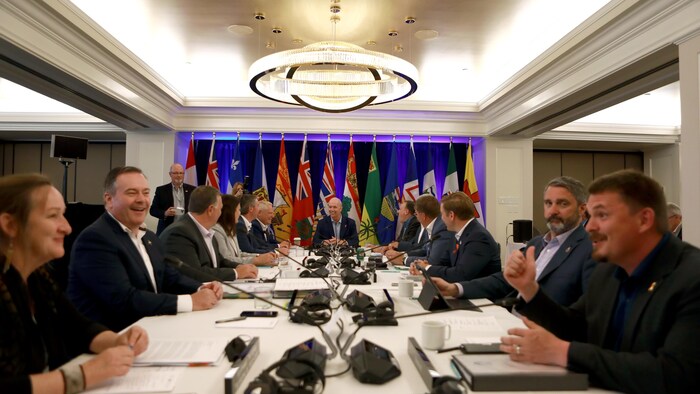 Les premiers ministres assis à une table, avec les drapeaux des provinces et territoires en arrière-plan.