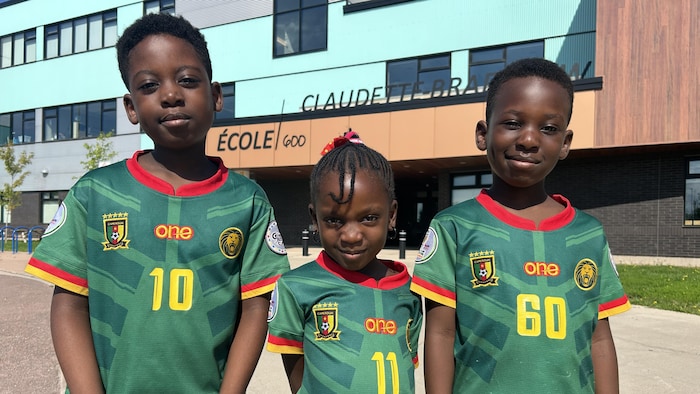 Trois enfants arrêtés devant une école. 