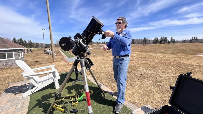 Un homme dehors prépare son télescope à l'approche d'une éclipse.