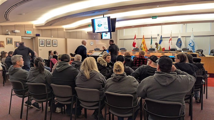 Des gens assis dans une salle du conseil municipal. 