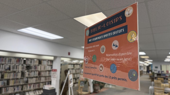 Une pancarte suspendue dans une bibliothèque détaille le service de prêt d'équipement sportif.