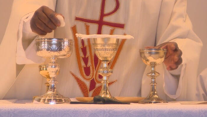 Plan sur les mains d'un prêtre qui tient, d'une main, des hosties et de l'autre, un verre.