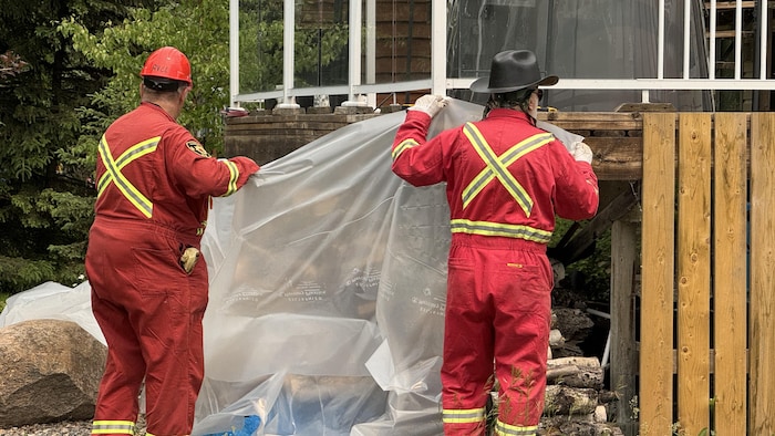 Firefighters put plastic around dry wood stored under a house by Candle Lake, in Saskatchewan, as part of the Firemart program to protect the dwellings from a forest fire, on June 10, 2025. state emergency lifted saskatchewan after