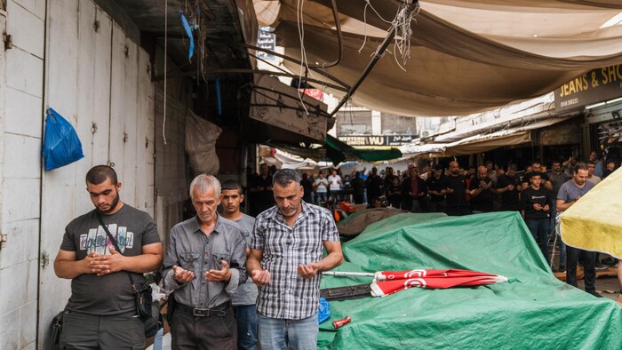 Des dizaines d'hommes prient côte à côte, debout dans une rue du marché.