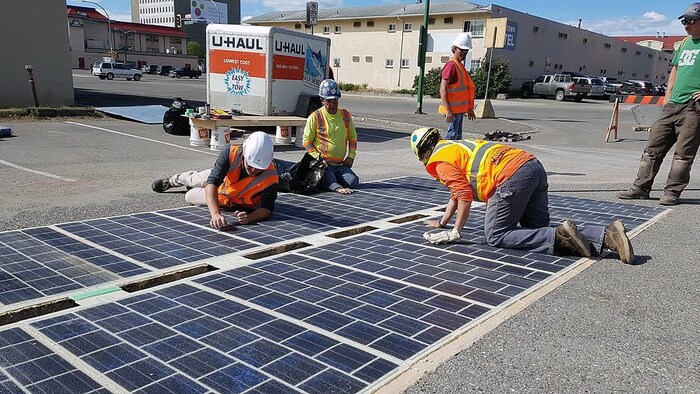 Des ouvriers sont à genoux sur les panneaux solaires qu'ils sont en train d'installer sur la chaussée.