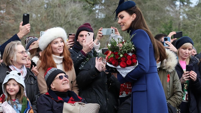 La princesse Kate, bouquets à la main, va à la rencontre du public qui lui sourit et la photographie lors d'une sortie.