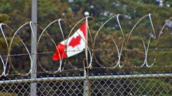 Un drapeau du Canada derrière des fils barbelés.