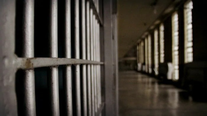 Le corridor d'une prison avec à gauche un gros plan sur les barreaux d'une cellule.