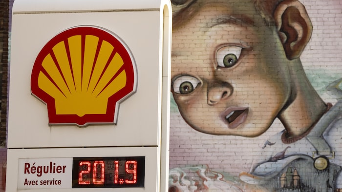 Une station-service affichant le prix de l'essence avec une murale à l'arrière-plan.