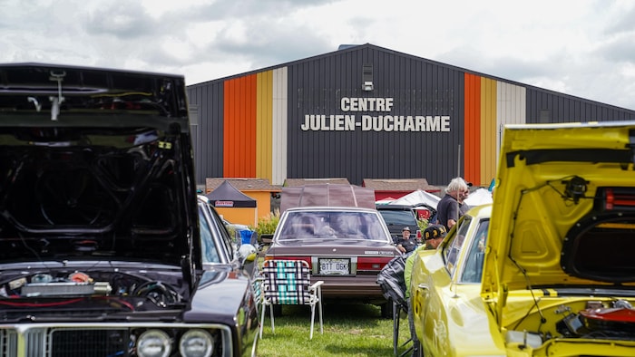 Des personnes se promènent au travers d'une exposition de voitures anciennes et sportives.