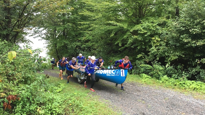 Une équipe de rameurs transporte un canot sur un sentier.