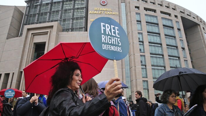 Une femme tient une petite pancarte qui porte la mention : « Défenseurs des droits de la personne » en anglais.