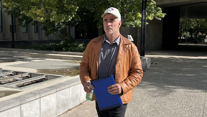 Dean Marchant qui marche sur le trottoir avec un dossier dans les mains, le 8 octobre 2026.