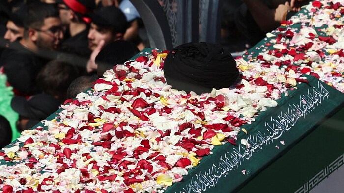 un cercueil est couvert de fleurs et orné de l'emblématique turban noir du guide suprême.