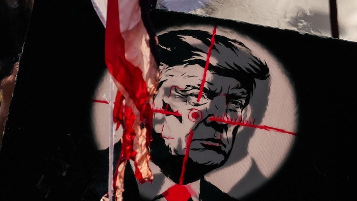 Un drapeau américain brûle devant une photo du président américain dans le viseur d'une arme.