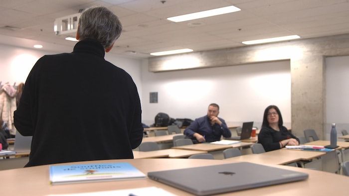 A UQAM teacher, seen from behind, conducts a lesson in front of a small group of teaching students.