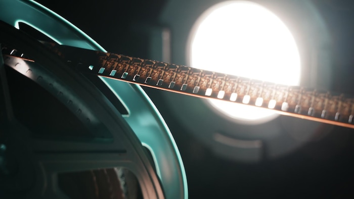 Une bobine de movie Super 8 devant un projecteur en gros program dans un environnement sombre.