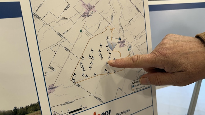 Une main pointe des éoliennes sur une carte.
