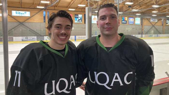Deux jeunes hommes en uniforme de hockey devant une glace dans un aréna.