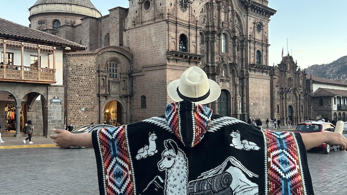 Une personnes vêtue d'une chapeau de paille et d'un poncho péruvien admire un monument à Cusco.