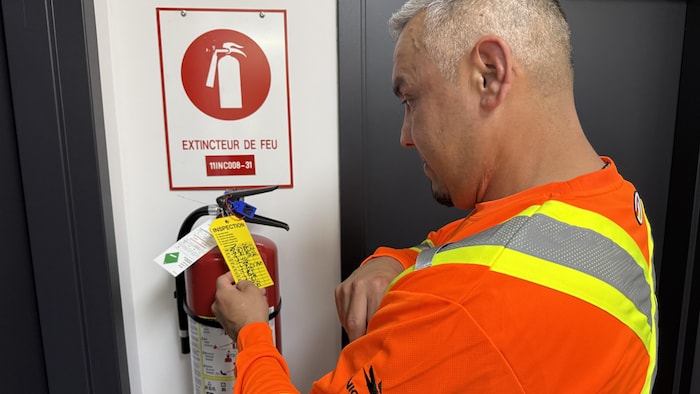 Jordan Kistabish inspecte un extincteur en consultant un petit carton.