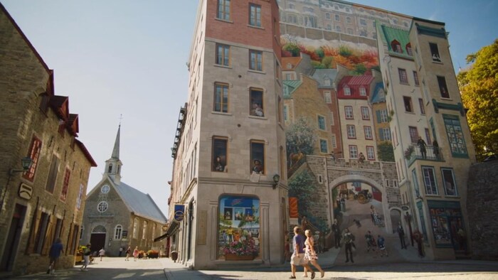 Deux personnes marchent devant une immense murale située près de la Place royale à Québec.