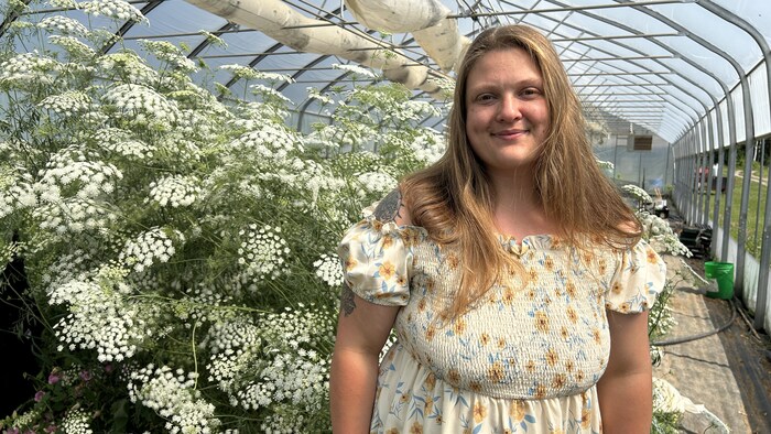 Une femme aux cheveux long et avec une robe sourit dans une serre florale.