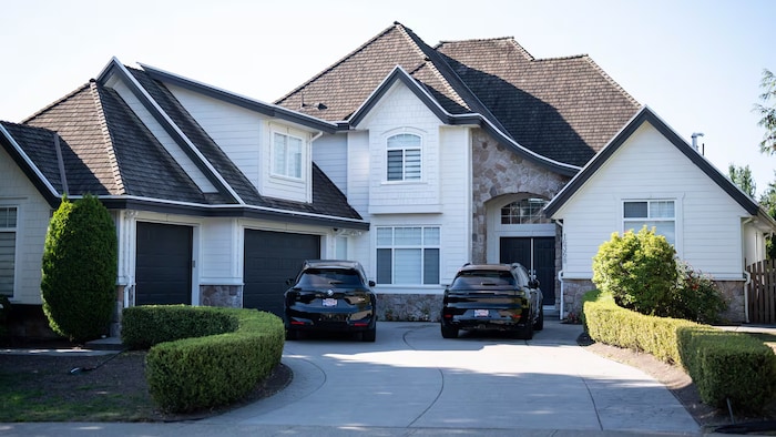 Une maison cossue et deux voitures noires garées devant.