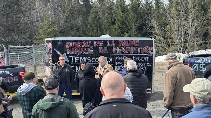 Une vingtaine de personne écoutent quatre élus devan tune roulotte taguée «bureau de la faune menacé de fermeture».