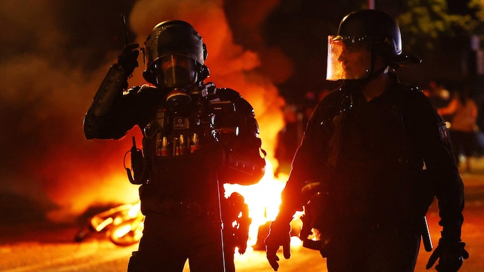 Des policiers dans la rue marchent devant des flammes.