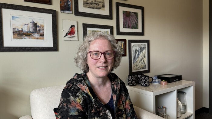 Charity Lui est assise dans son cabinet de consultation. Le mur derrière elle est couvert de tableaux et d'aquarelles colorées.