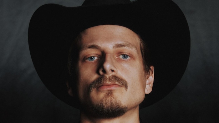 Le chanteur airs avec un chapeau de cowboy et une chemise avec des têtes de mort et des fleurs.