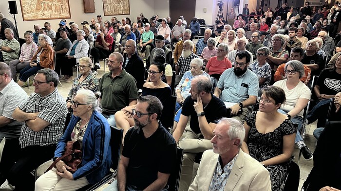 Un public d'environ 120 personnes assises dans une salle assiste à une séance d'information.