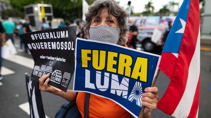 A protester holds a sign saying 'LUMA Out' during a 2021 march in San Juan, Puerto Rico. Demonstrations against the Canadian-led power company and its 15-year, $2-billion contract are part of daily life on the island. (Carlos Giusti/The Associated Press)