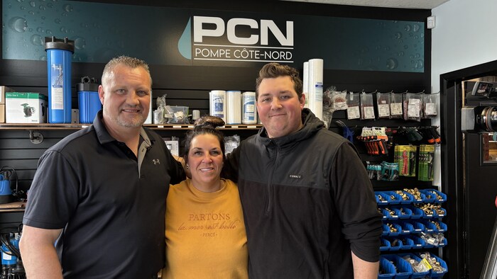Un homme, une femme et un jeune homme posent pour la caméra devant des étagères pleines d'équipements.