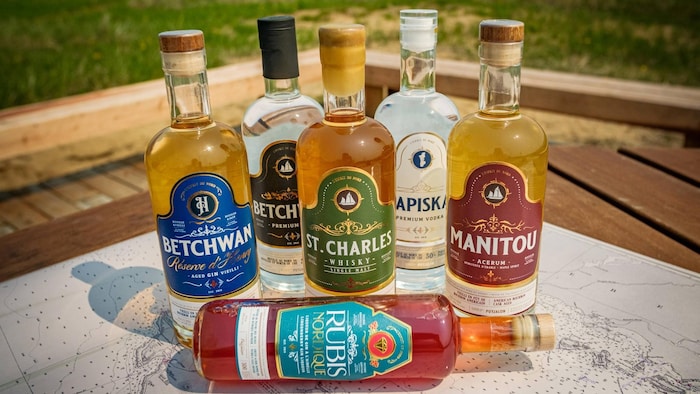 Six bouteilles de spiritueux de la distillerie Puyjalon sont disposées sur une carte géographique de la Minganie, dehors.