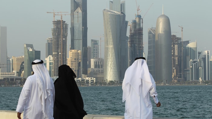 Deux hommes et une femme marchent au bord de la mer près de Doha, au Qatar. 