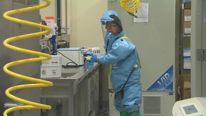 Une femme dans un laboratoire porte une combinaison de haute sécurité.