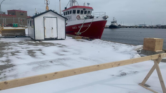 Une barricade de bois placée sur un quai auquel un bateau de pêche est amarré.