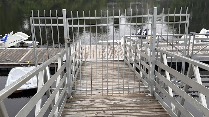 Une barrière métallique ferme l'accès à un quai flottant où sont amarrées des embarcations.