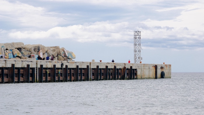 Vue de côté de l'infrastructure qui pointe vers le large. Deux personnes pêchent au bout.