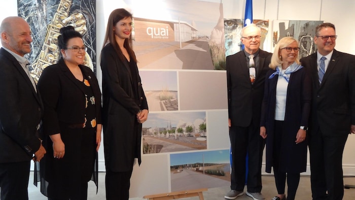 Six personnes posent près d'un panneau présentant des dessins d'architectes pour le projet de quai. 