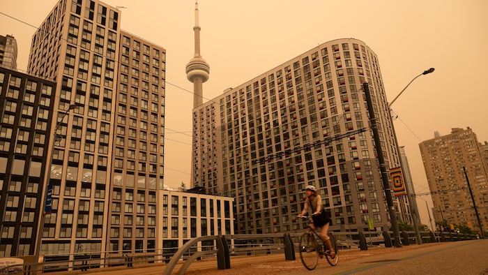 Une personne se déplace en vélo sur le bord de l'eau de Toronto. On voit la Tour CN loin à l'arrière.